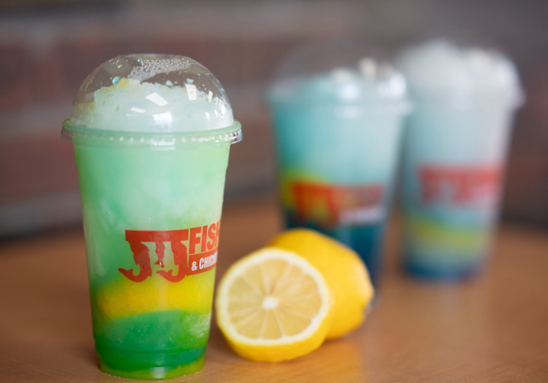 Cups of JJ Fish & Chicken fresh-squeezed lemonade in bright layered green, yellow, and blue with sliced lemons